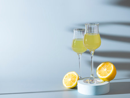 Limoncello, traditional Italian liquor on a light concrete background in the rays of the sun. Next...