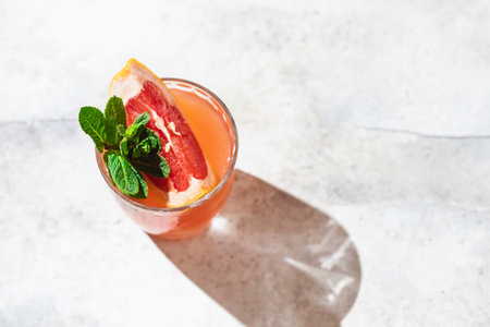 A glass of freshly squeezed grapefruit juice and mint on a light gray concrete background. Refreshing summer cocktail. Selective focus, copy spaceの写真素材