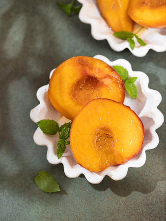 Caramelized peaches with honey, with mint leaves on a concrete background with shadows. Summer dessert.の写真素材
