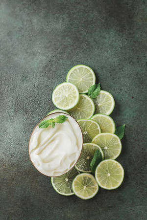 Jar with cosmetic product with lime and mint halves on green concrete. Natural citrus cosmetics with vitamin C. Copy space.の写真素材