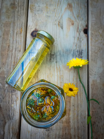 Bottles and dried calendula officinalis petals with macerated oil on wooden background.