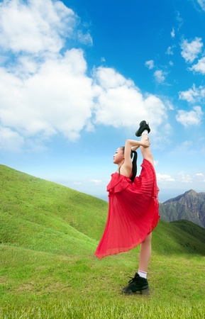 Pretty girl wearing a red dress, dancing in the mountains.の写真素材