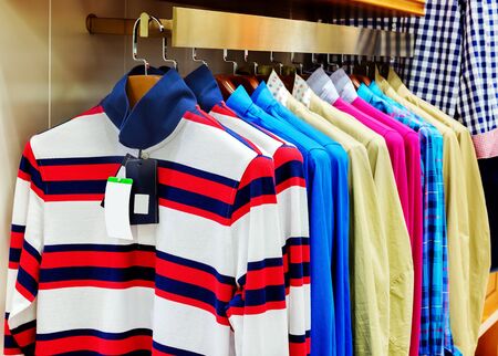 A row of colorful row t-shirts hanging on hangersの写真素材