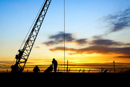Construction site, silhouettes of construction industry workers on scaffolding against the sunset light.の写真素材