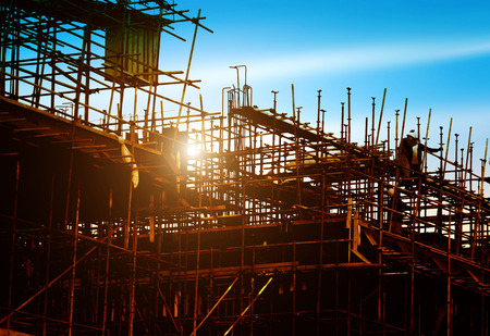 Construction site, silhouettes of construction industry workers on scaffolding against the sunset light.のeditorial素材