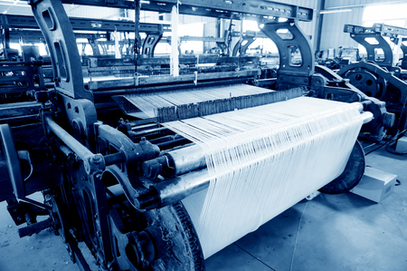 A row of textile looms weaving cotton yarn in a textile mill.の写真素材