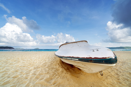 Fishing boat on a sandy beach with blue ocean and summer skyの写真素材