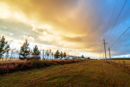 At dusk, the car is driving in the grasslands.の写真素材
