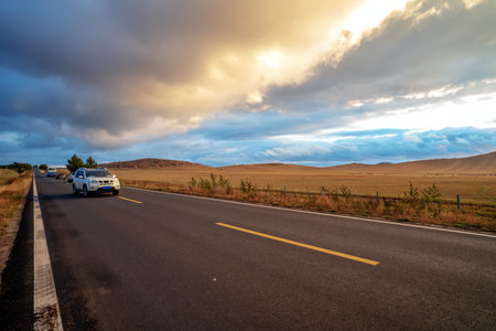 At dusk, the car is driving in the grasslands.の写真素材