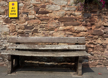 empty bench with a sign stating no parking at any time on the wall of a house in cockington village...