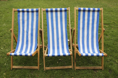 three blue and white stripped empty deckchairs in a park 
