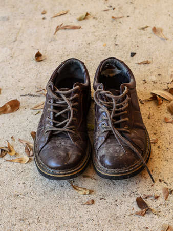 Old and dirty men brown leather shoes with dry leaves on concrete floorの写真素材