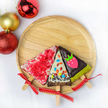 Home made brownies winter tree shape with red bow and ribbon on wooden plate; christmas glitter ball on white backgroundの写真素材