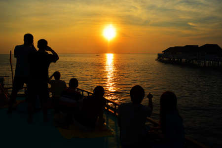 Silhouette of couple lovers and tourist watching the sun setting on cruise over sea.の写真素材