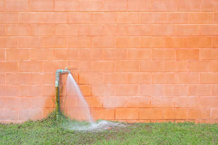Old outside faucet and heavy water flow with new orange brick wallの写真素材