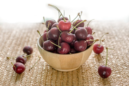 Cherries with water drops in wooden bowl on natural weaving background