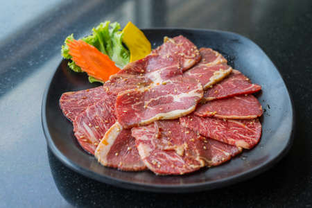 Raw beef slice for barbecue or Japanese style yakiniku on black plate.の写真素材