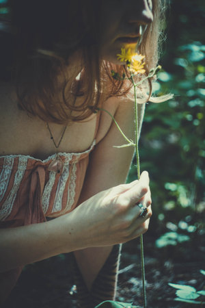 Close up woman with flower concept photo. Lady and wildflower. Side view photography with green forest on background. High quality picture for wallpaper, travel blog, magazine, articleの写真素材