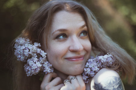 Close up happy woman pressing lilac stems to face portrait picture. Garden time. Closeup front view photography with blurred background. High quality photo for ads, travel blog, magazine, articleの写真素材