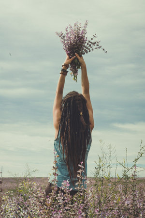 Woman raising up bouquet in field scenic photography. Picture of person with cloudy sky on background. High quality wallpaper. Photo concept for ads, travel blog, magazine, articleの写真素材