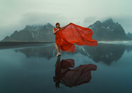 Graceful woman wrapped with red chiffon on beach scenic photography. Picture of person with...