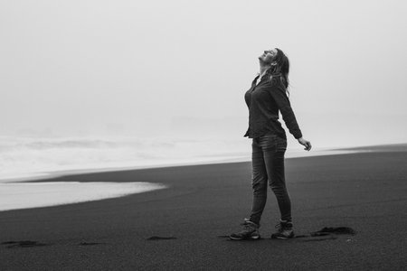 Inspiring lady on wild Reynisfjara monochrome scenic photography. Picture of person with stormy sea on background. High quality wallpaper. Photo concept for ads, travel blog, magazine, articleの写真素材