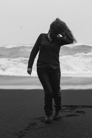 Traveler walking along on Reynisfjara beach monochrome scenic photography. Picture of person with rough sea on background. High quality wallpaper. Photo concept for ads, travel blog, magazine, articleの写真素材