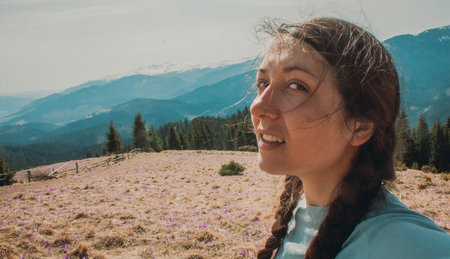 Close up young woman with disheveled hair looking sideways portrait picture. Closeup side view photography with mountain peak on background. High quality photo for ads, travel blog, magazine, articleの写真素材