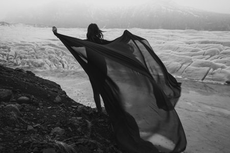 Graceful lady with waving fabric sheet monochrome scenic photography. Picture of person with high glacier on background. High quality wallpaper. Photo concept for ads, travel blog, magazine, articleの写真素材