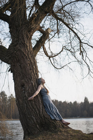 Reconnection with nature scenic photography. Picture of beautiful authentic lady in dress with lake, willow on background. High quality wallpaper. Photo concept for ads, travel blog, magazine, articleの写真素材