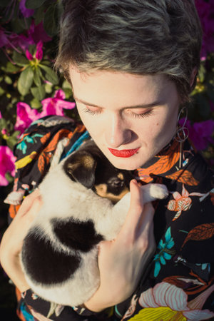 Close up woman with haircut holding puppy in garden portrait picture. Closeup front view photography with blossom on background. High quality photo for ads, travel blog, magazine, articleの写真素材