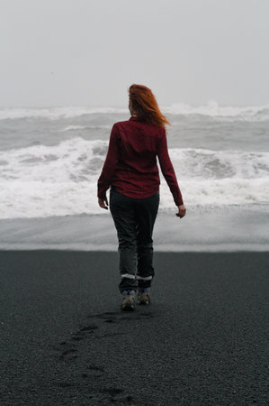 Tourist spending time on Reynisfjara beach scenic photography. Picture of person with splashing sea waves on background. High quality wallpaper. Photo concept for ads, travel blog, magazine, articleの写真素材