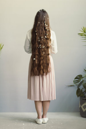 Close up young woman with white petals in long hair concept photo. Back view photography with wall...