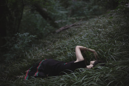 Lying in dark forest thick grass scenic photography. Picture of young sleepy woman with deep...