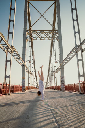 Handstand on pathway bridge scenic photography. Picture of woman in white shirt with steel structures on background. High quality wallpaper. Photo concept for ads, travel blog, magazine, articleの写真素材