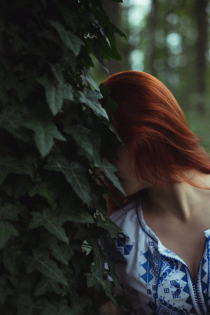 Close up ginger haired woman pressing head against ivy leaves concept photo. Side view photography...
