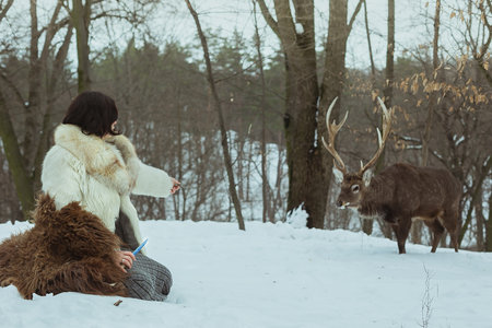 Snowy fantasy aesthetic scenic photography. Picture of woman in fur coat and stag with woodland on background. High quality wallpaper. Photo concept for ads, travel blog, magazine, articleの写真素材