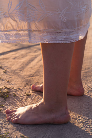 Close up female bare feet standing on sand concept photo. Cozy sunset aesthetic. Side view photography with blurred background. High quality picture for wallpaper, travel blog, magazine, articleの写真素材