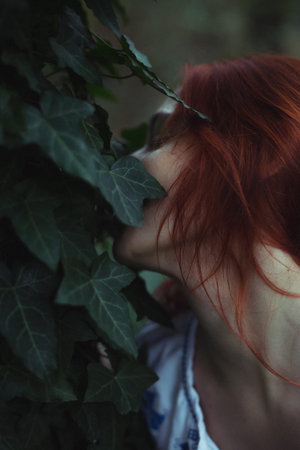 Close up woman with closed eyes hiding face in ivy leaves concept photo. Side view photography with...