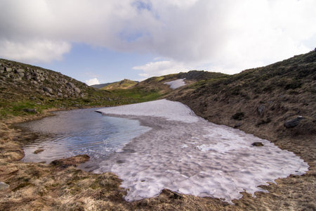 Melting ice puddle in spring mountains landscape photo. Beautiful nature scenery photography with sky on background. Ambient light. High quality picture for wallpaper, travel blog, magazine, articleの写真素材