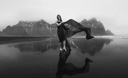 Pretty woman on Reynisfjara beach monochrome scenic photography. Picture of person with hills on background. High quality wallpaper. Photo concept for ads, travel blog, magazine, articleの写真素材