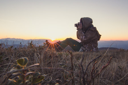 Hiker photographer making shot of sunset in mountains scenic photography. Picture of traveler with landscape. High quality wallpaper. Backlight photo concept for ads, travel blog, magazine, articleの写真素材
