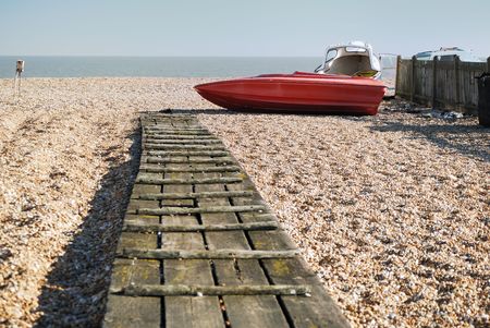 Walkway on a beach leading to an old speed boatの写真素材