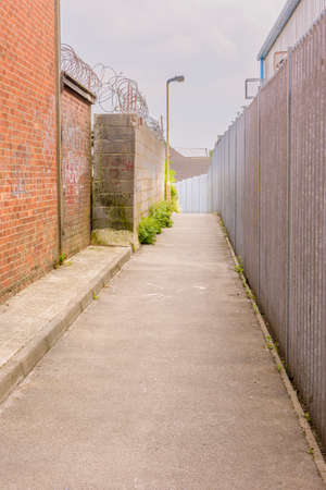 Alleyway and fence passing at the side of industrial buildingsの写真素材