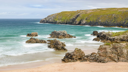 Bay with golden sand with the ocean around rocks in the water
