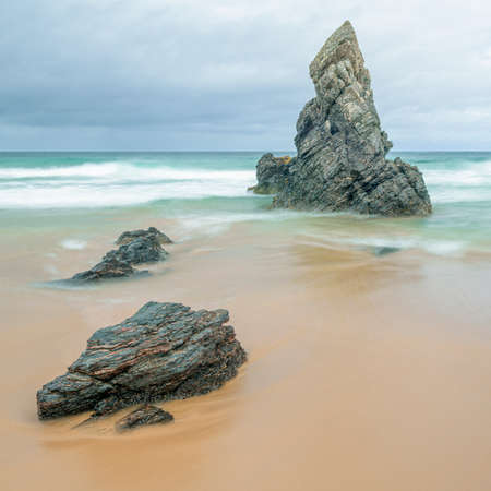 Sea stack and rocks on a golden beach as the tide comes inの写真素材