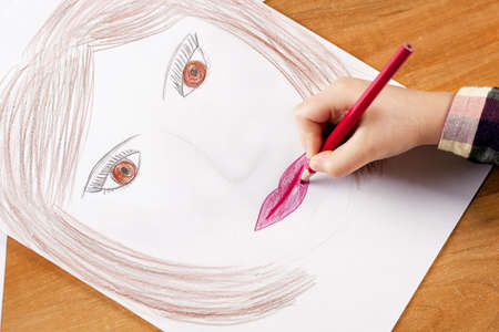 child s hand with the pencil drawing the moter s portrait on a white sheet of paperの写真素材