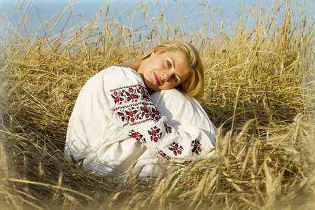 young blonde women sitting on a the field of wheat ears in national dressの写真素材