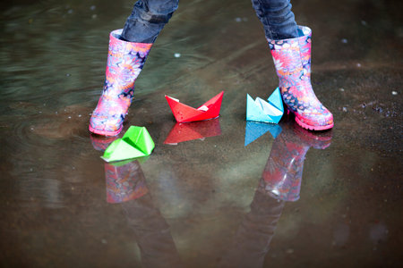 Variegated rain boots in puddle with colorful paper ship