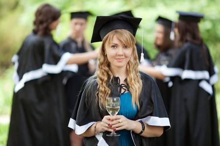 Bachelor graduates celebrate with a glass of white wine in mantlesの写真素材